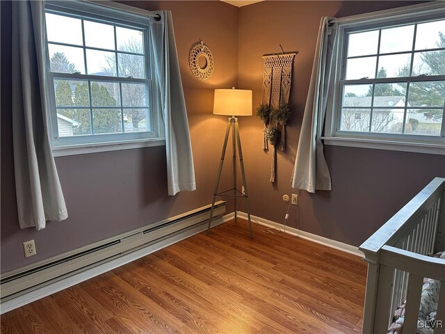 unfurnished bedroom with baseboard heating, a nursery area, and hardwood / wood-style flooring