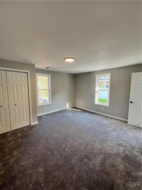 unfurnished bedroom with multiple windows, a closet, and dark colored carpet