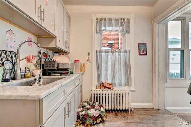 kitchen with radiator, light stone countertops, sink, and white cabinets