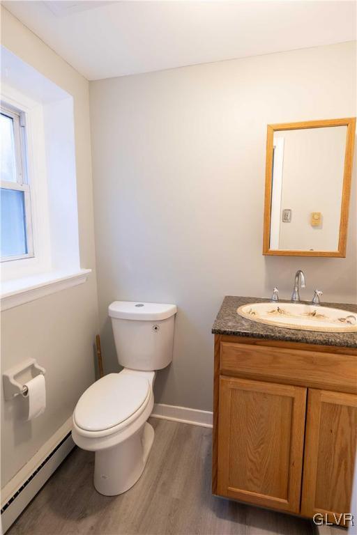 bathroom featuring wood-type flooring, vanity, baseboard heating, and toilet