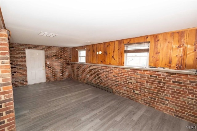 spare room with dark wood-type flooring, wood walls, and brick wall