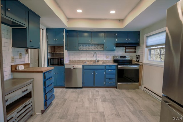 kitchen featuring blue cabinetry, sink, stainless steel appliances, baseboard heating, and a raised ceiling