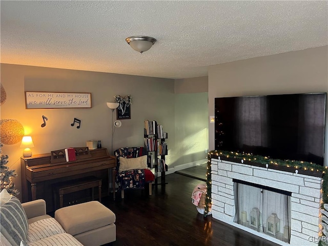 living room with dark hardwood / wood-style floors, a stone fireplace, and a textured ceiling