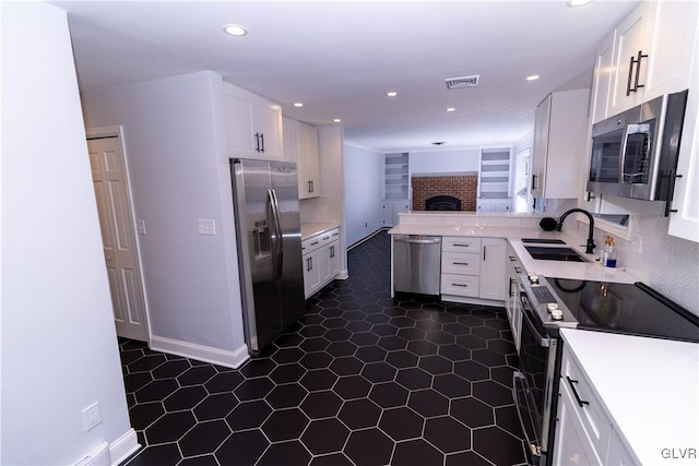 kitchen featuring kitchen peninsula, appliances with stainless steel finishes, sink, a fireplace, and white cabinetry