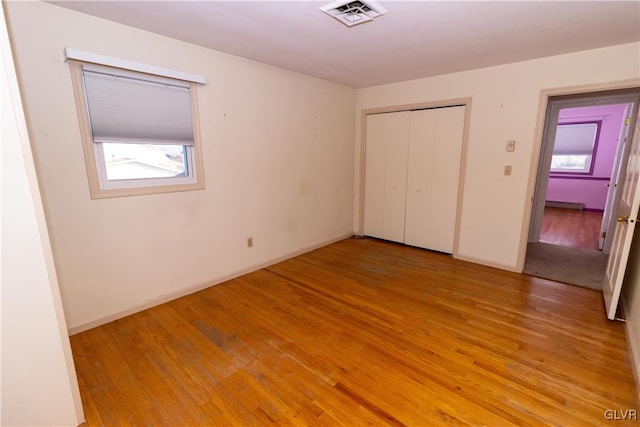 unfurnished bedroom featuring baseboard heating, a closet, light hardwood / wood-style flooring, and multiple windows