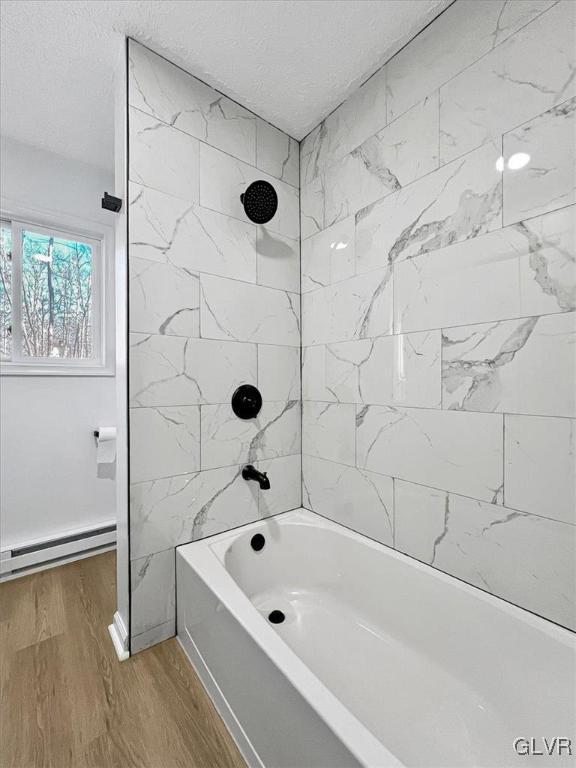 bathroom with a textured ceiling, wood-type flooring, a baseboard heating unit, and tiled shower / bath