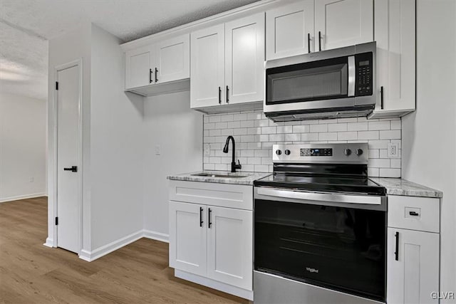 kitchen with light stone countertops, appliances with stainless steel finishes, sink, white cabinets, and light hardwood / wood-style floors