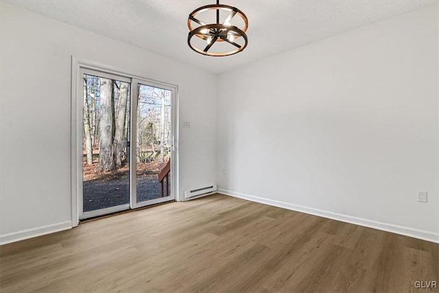 empty room with hardwood / wood-style floors, a textured ceiling, baseboard heating, and a notable chandelier