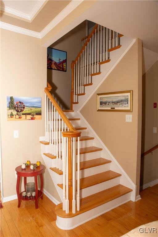 staircase with wood-type flooring and ornamental molding