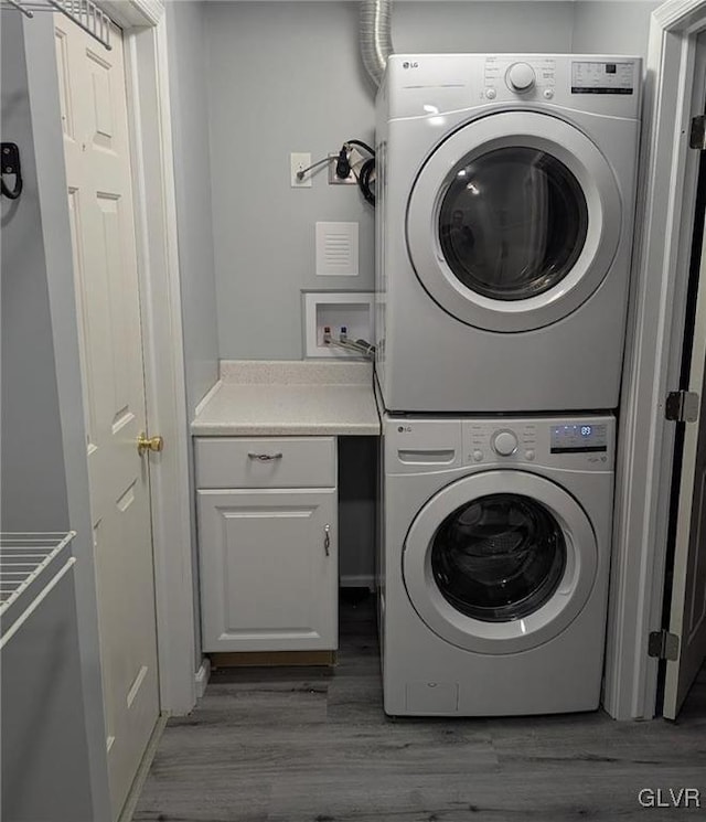 laundry area with dark hardwood / wood-style floors, cabinets, and stacked washing maching and dryer