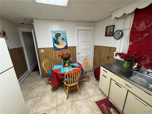 dining room featuring light tile patterned floors, a paneled ceiling, baseboard heating, and wooden walls