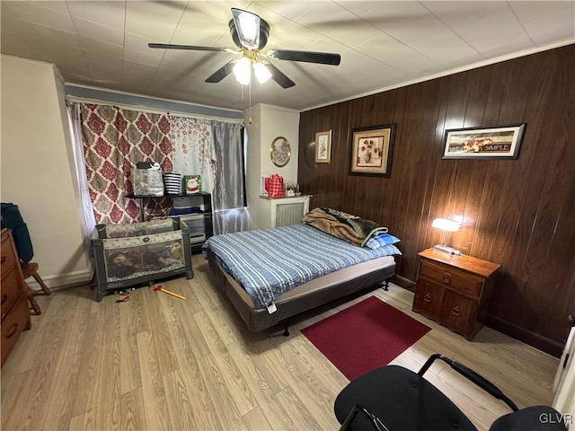 bedroom featuring ceiling fan, crown molding, light hardwood / wood-style floors, and wood walls