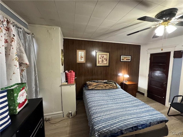 bedroom featuring ceiling fan, wood walls, light hardwood / wood-style floors, and ornamental molding