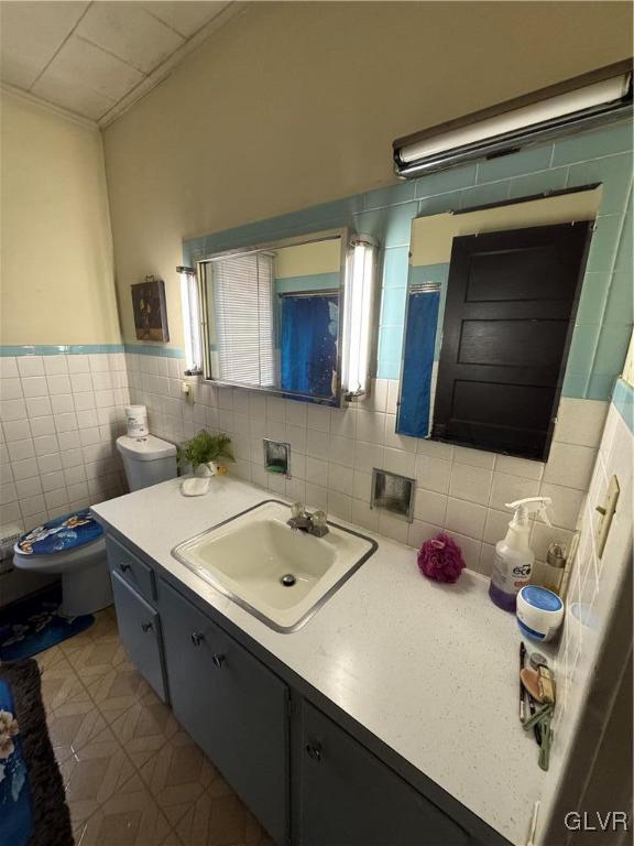 bathroom featuring tile patterned floors, toilet, vanity, tile walls, and ornamental molding