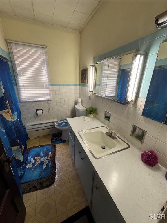 bathroom with vanity, toilet, tile walls, and a baseboard heating unit