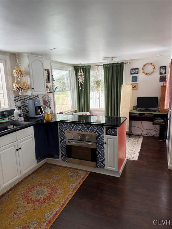 kitchen with white cabinetry, stainless steel oven, sink, dark hardwood / wood-style floors, and decorative backsplash