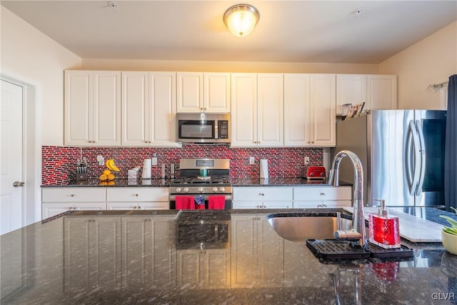 kitchen with appliances with stainless steel finishes, tasteful backsplash, sink, dark stone countertops, and white cabinets