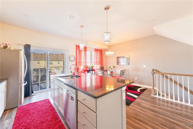 kitchen with appliances with stainless steel finishes, a kitchen island with sink, dark wood-type flooring, sink, and pendant lighting