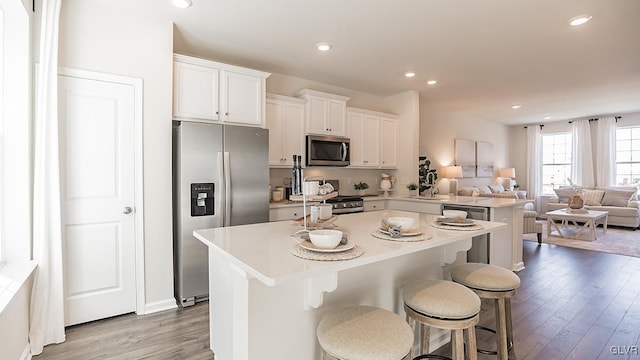 kitchen with stainless steel appliances, a breakfast bar area, white cabinetry, and light hardwood / wood-style flooring