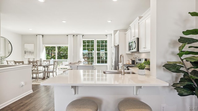 kitchen with stainless steel appliances, white cabinets, kitchen peninsula, a breakfast bar area, and dark wood-type flooring