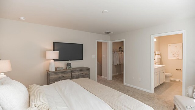 bedroom featuring a walk in closet, light colored carpet, a closet, and connected bathroom