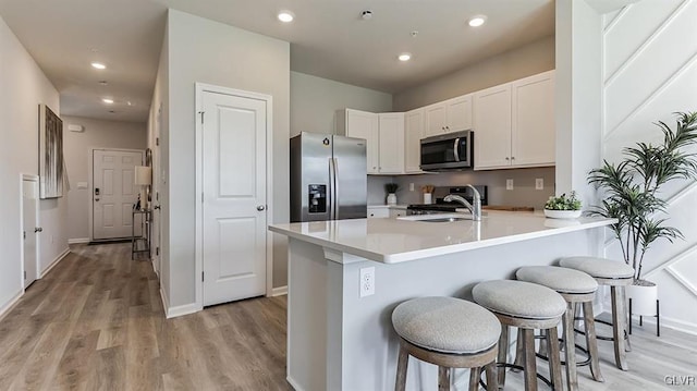 kitchen featuring white cabinets, light hardwood / wood-style floors, a kitchen bar, kitchen peninsula, and stainless steel appliances