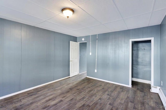 spare room with a drop ceiling, dark hardwood / wood-style floors, and a baseboard heating unit