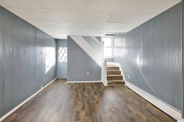 basement with dark hardwood / wood-style flooring, baseboard heating, and wooden walls