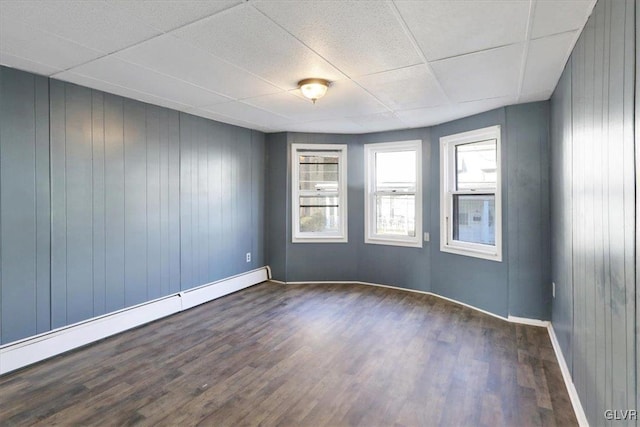 empty room featuring a drop ceiling, wood walls, dark hardwood / wood-style flooring, and baseboard heating