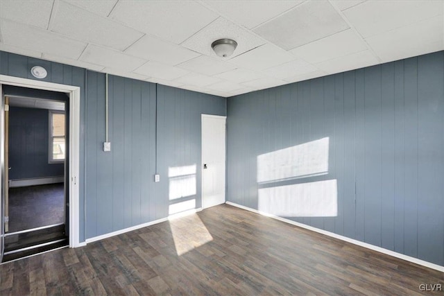 spare room with wood walls, dark wood-type flooring, and a baseboard heating unit