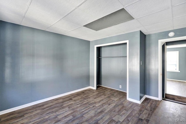 unfurnished bedroom featuring a paneled ceiling, dark hardwood / wood-style floors, and a closet