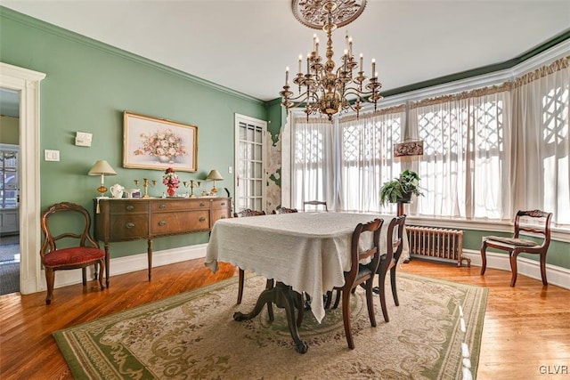 dining room with wood-type flooring, radiator heating unit, ornamental molding, and a notable chandelier