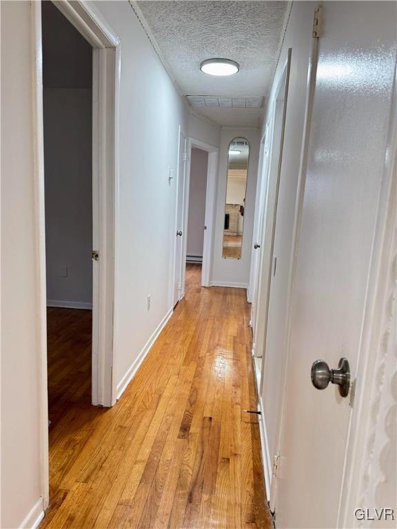 corridor with a textured ceiling and light wood-type flooring