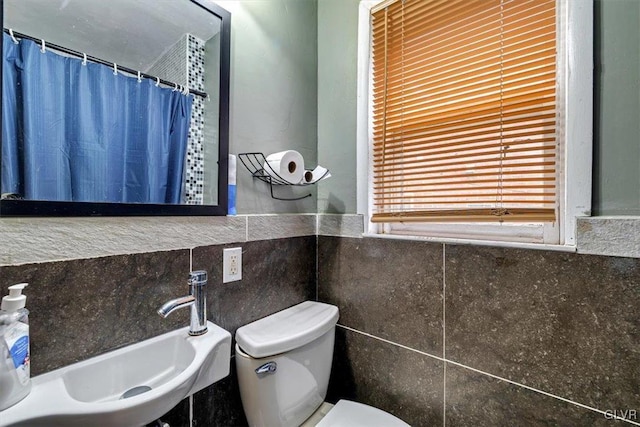 bathroom featuring a shower with curtain, sink, tile walls, and toilet