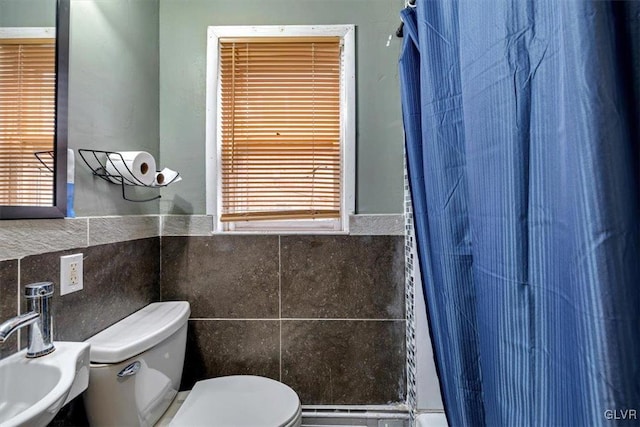 bathroom with toilet, curtained shower, sink, and tile walls