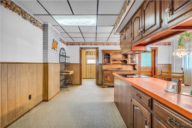 kitchen featuring a paneled ceiling, black electric stovetop, wooden walls, and an inviting chandelier