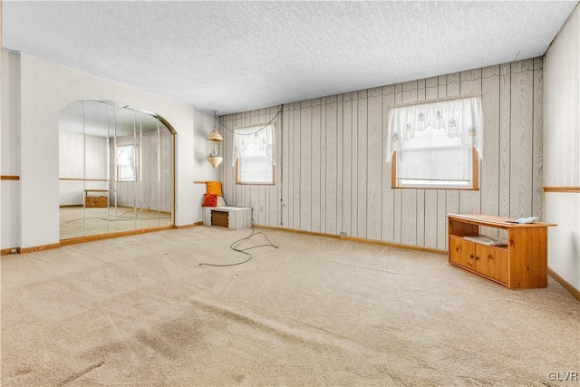 unfurnished room featuring wood walls, light colored carpet, and a textured ceiling