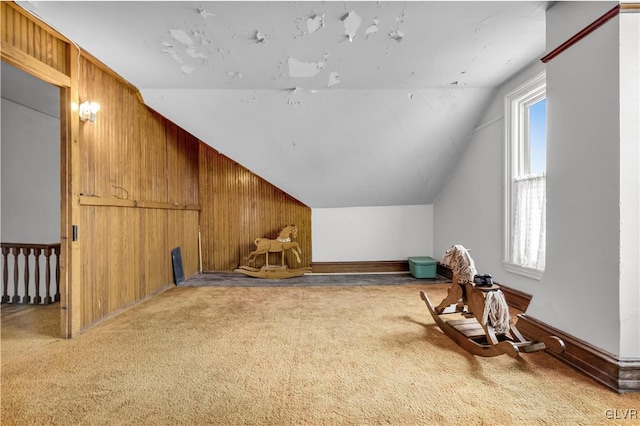 additional living space featuring wood walls, plenty of natural light, light carpet, and lofted ceiling