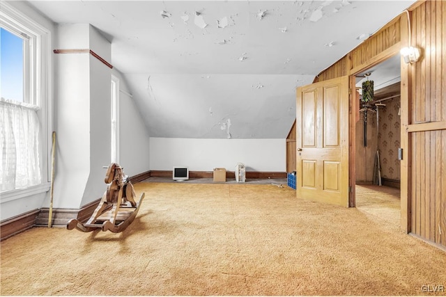 additional living space with carpet, wooden walls, vaulted ceiling, and a healthy amount of sunlight