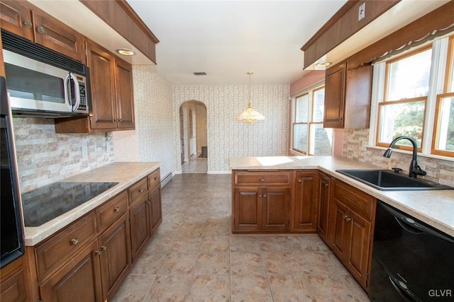 kitchen featuring sink, kitchen peninsula, pendant lighting, decorative backsplash, and black appliances