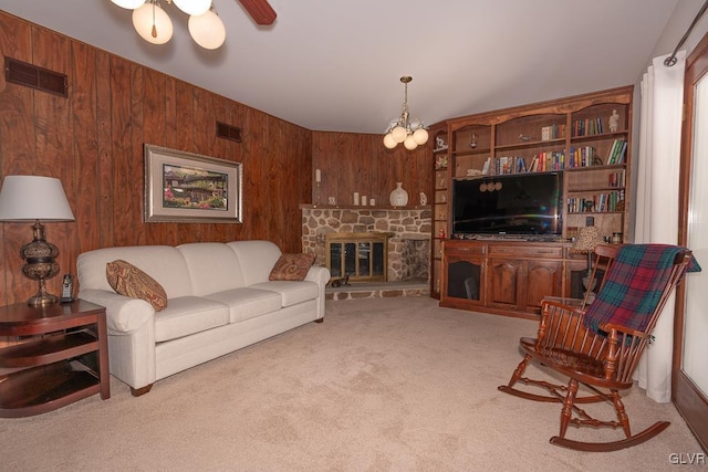 living room featuring light carpet, ceiling fan with notable chandelier, a stone fireplace, and wood walls