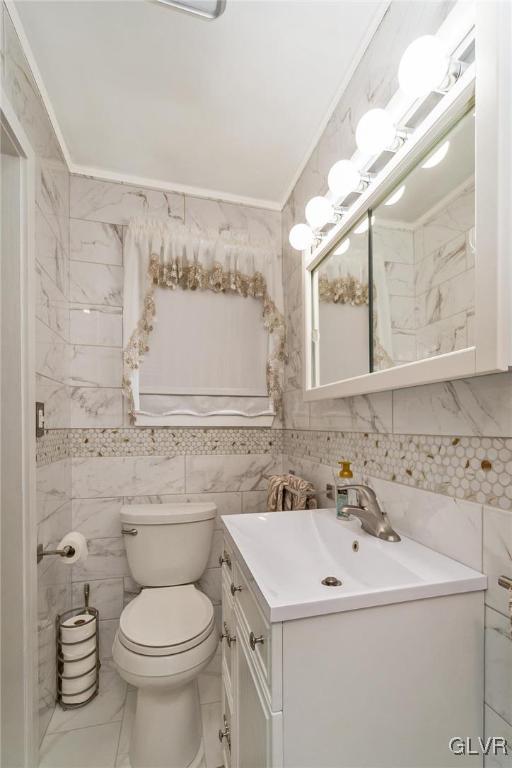 bathroom featuring toilet, vanity, tile walls, and ornamental molding