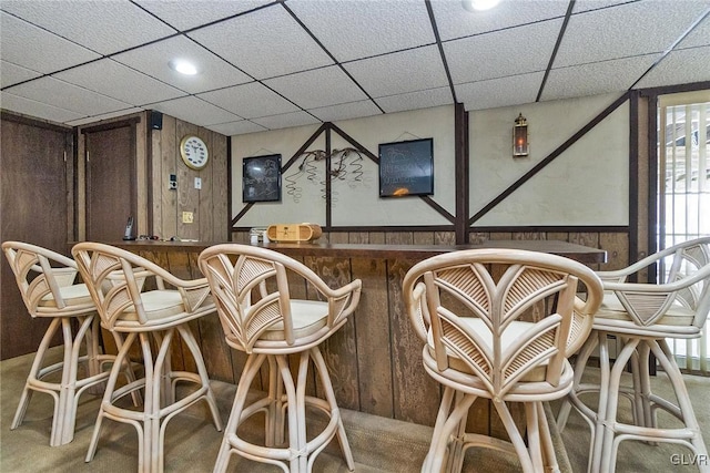 bar featuring a drop ceiling, carpet floors, and wood walls