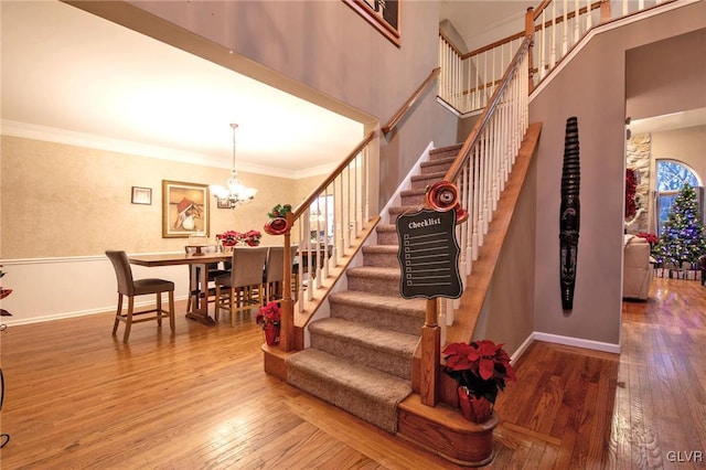 stairway featuring baseboards, crown molding, hardwood / wood-style floors, and an inviting chandelier