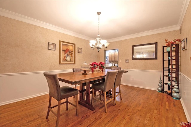 dining area featuring crown molding, a wainscoted wall, a notable chandelier, and wood finished floors