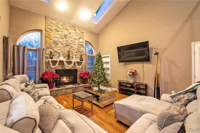 living area featuring a skylight, plenty of natural light, wood finished floors, and a stone fireplace