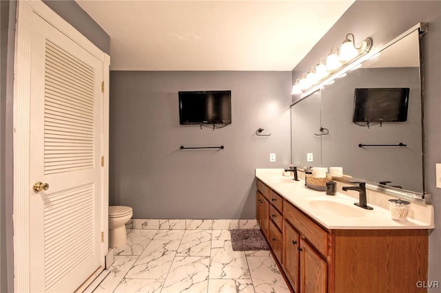 bathroom featuring toilet, marble finish floor, double vanity, and a sink