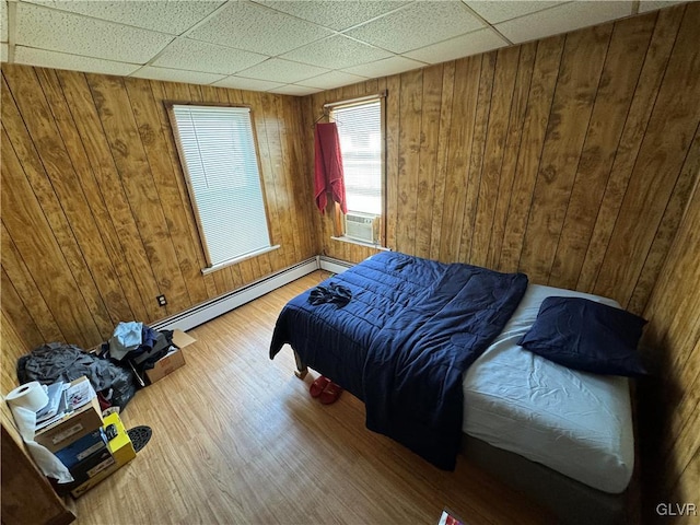 bedroom featuring wood walls, wood-type flooring, and a baseboard radiator