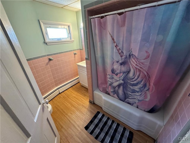 bathroom featuring shower / bath combination with curtain, a drop ceiling, wood-type flooring, a baseboard radiator, and tile walls