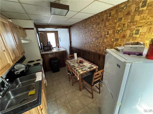 kitchen featuring a drop ceiling, sink, white fridge, wooden walls, and light tile patterned floors